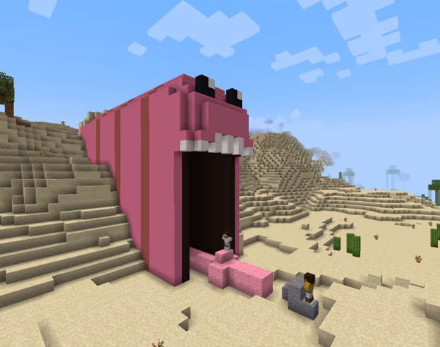 Image created in Minecraft of a large pink worm with a wide open mouth and large tongue coming out that's emerging from a giant desert sand block wall