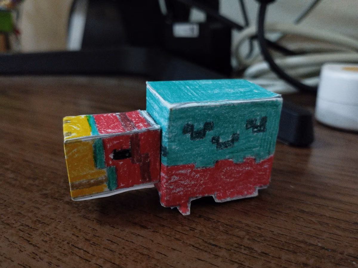 Photo of a papercraft cubed four legged creature with a burgundy body, yellow nose, and teal top layer. 