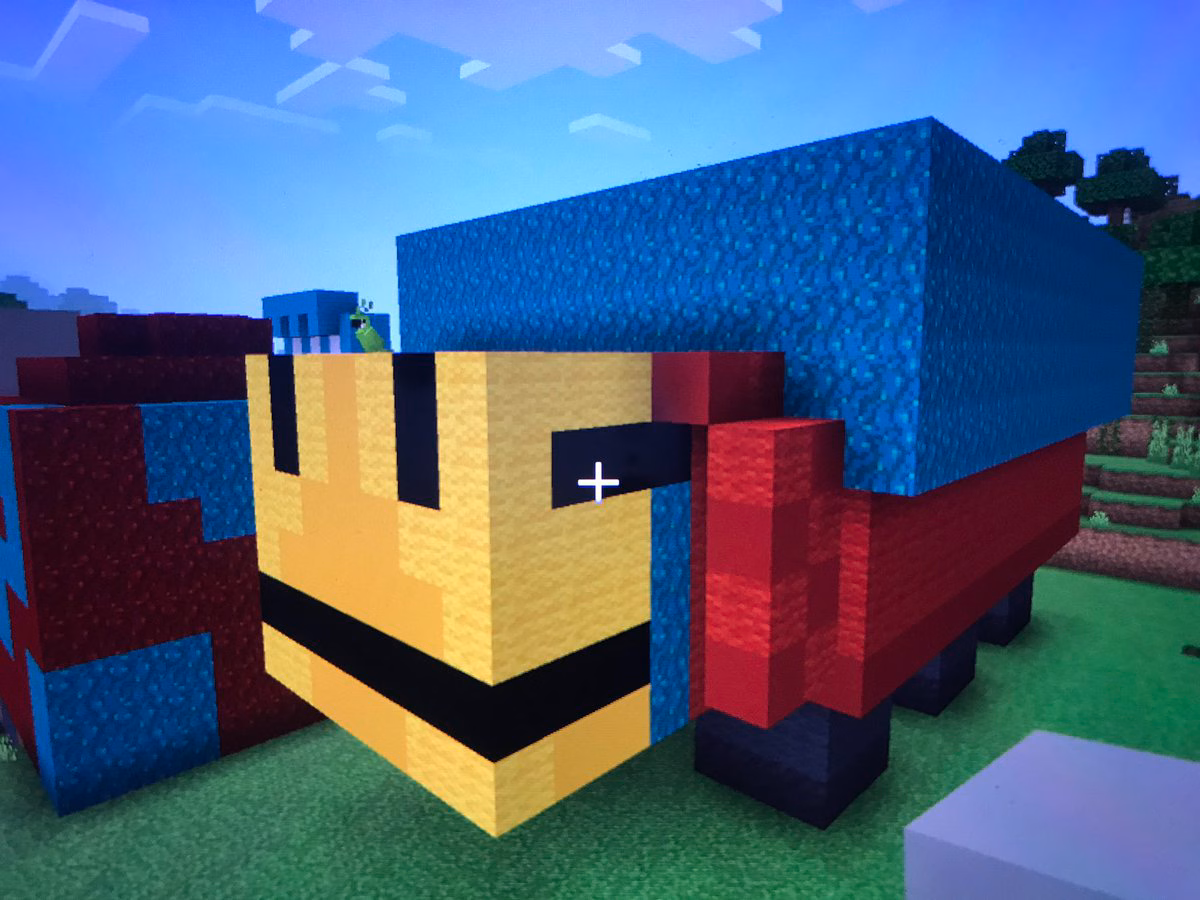 Image from Minecraft of a rectangular four legged creature made out of burgundy blocks, yellow blocks for the nose, and topped with teal blocks. 