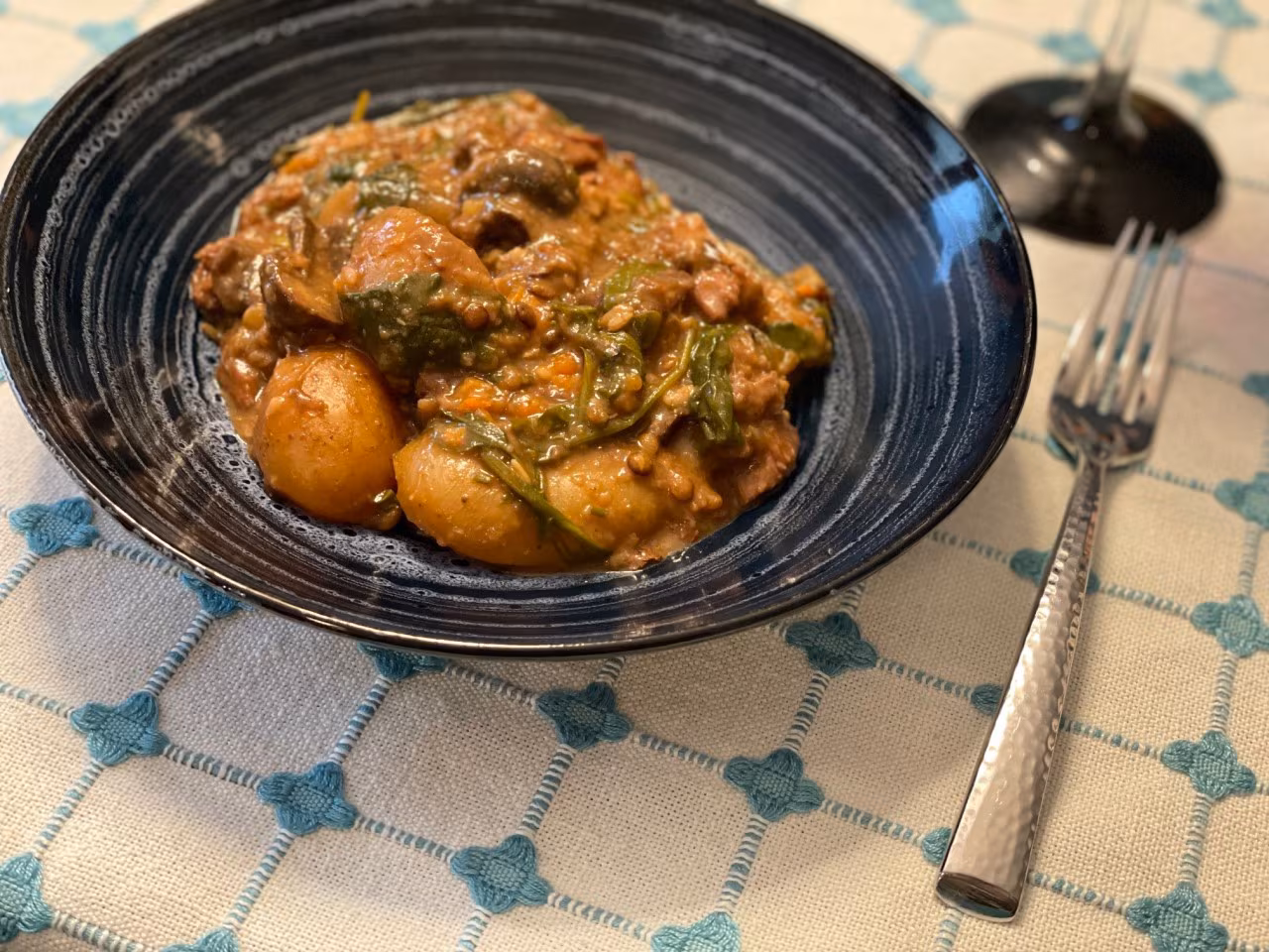 Photo of a chunky vegetable stew in a black bowl sitting atop of a table