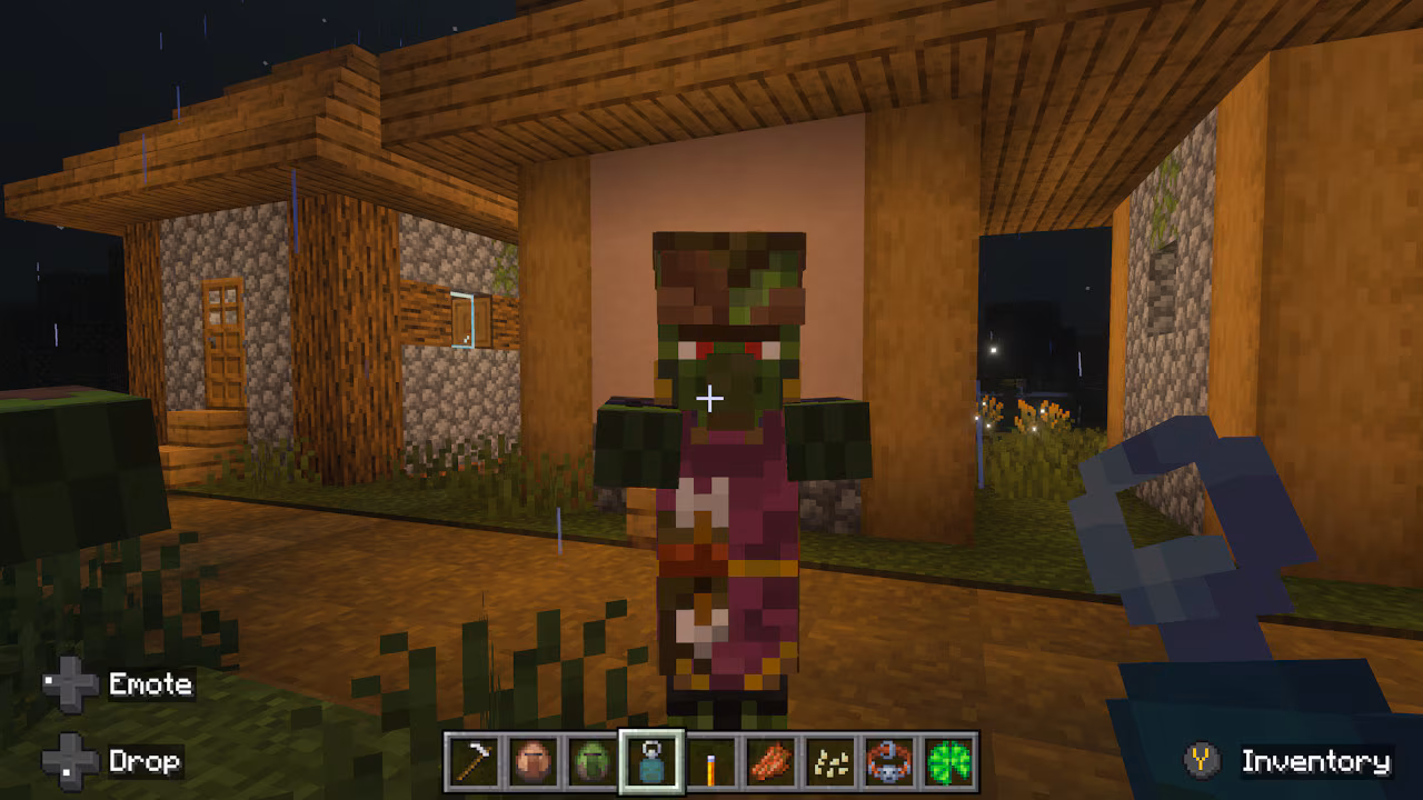 A zombie villager stands outside a house at night. The player holds a blue key-like item.