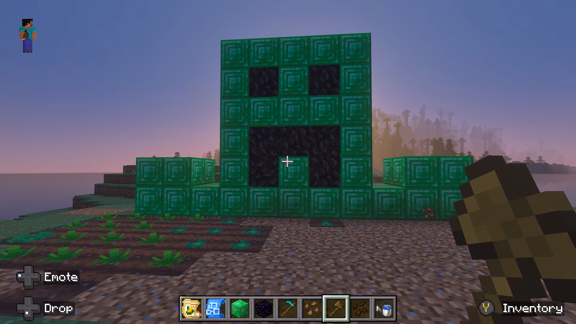 A large pixel-art face made from green and dark blocks stands beside farmland with newly planted crops at sunrise.