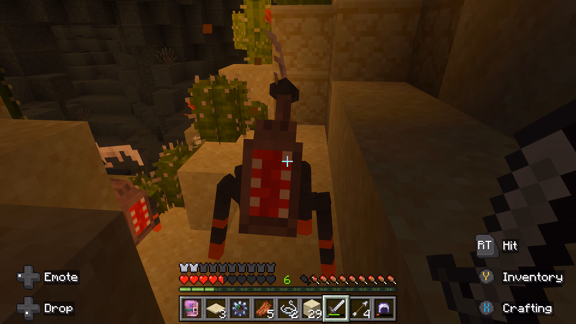 Minecraft player confronts a large red-and-black insect-like creature among cacti and sandy blocks in an underground cave.
