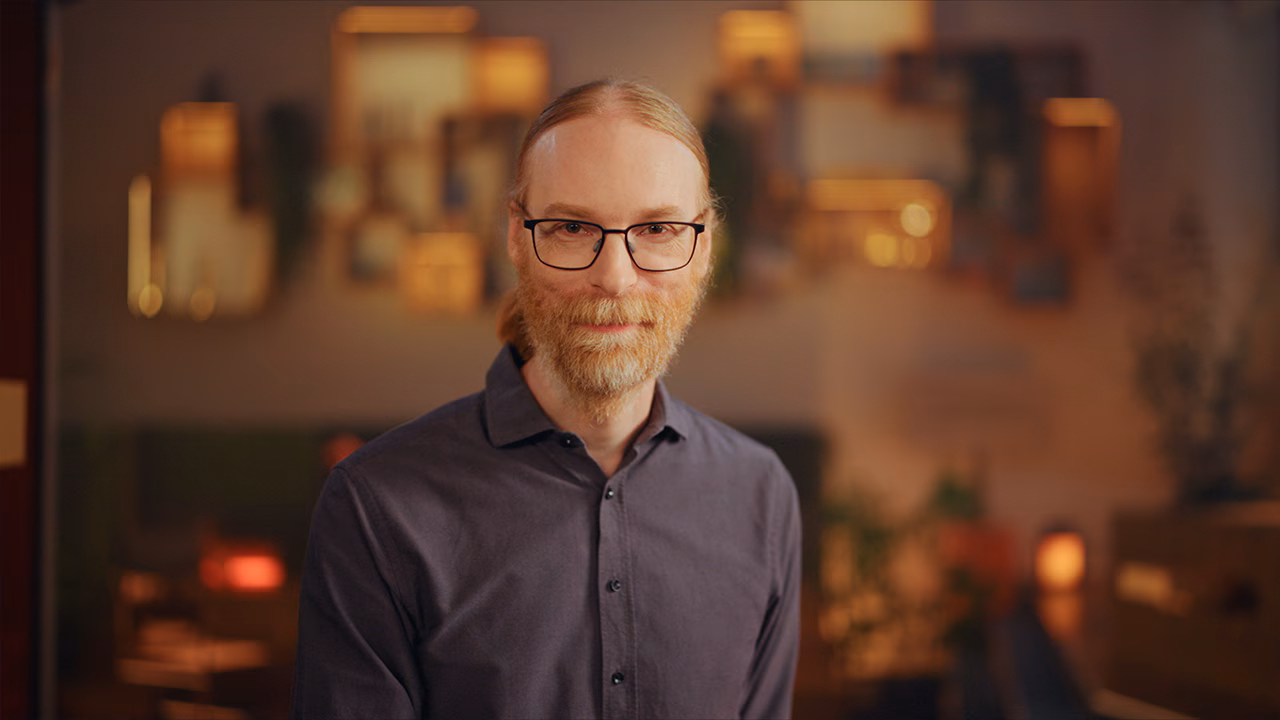 Portrait of a bearded man, Jens Bergenström, wearing glasses, standing against a softly lit background.