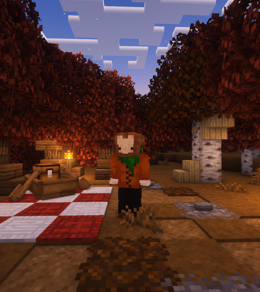 Image of a character in Minecraft with a head that looks like a slice of toast wearing a cardigan style sweater with a green scarf standing in a autumn field with a red checkered picnic blanket and boat with a chest inside. 